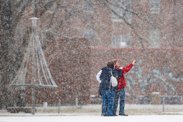 Photo of snow falling down on couple taking selfie on the Oval with a Christmas tree in the back ground. 